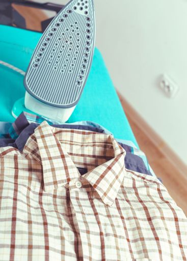Iron on ironing board on light home interior background