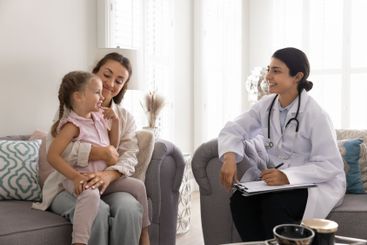 Happy Indian doctor visiting little patient girl and her...