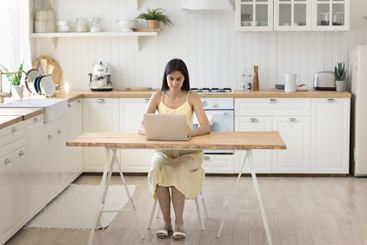 Young woman working on notebook at home office in kitchen