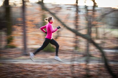 young woman running outdoors in a city park on a cold...