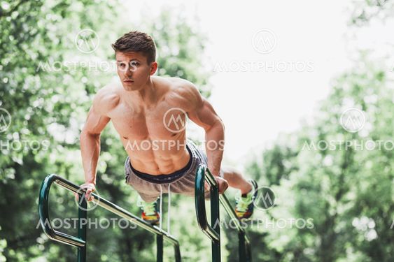 Young fit man doing push ups on bars