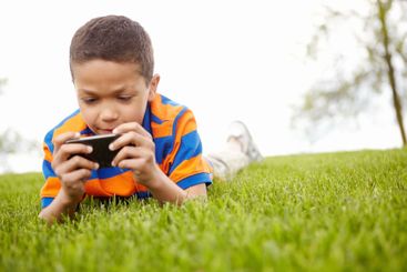 Little boy, lawn and playing with phone for video games,...