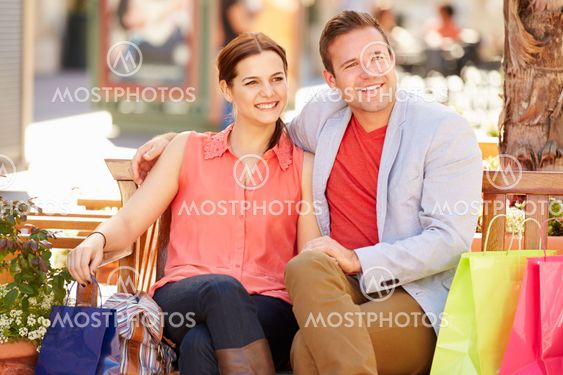 Young Couple Resting With Shopping Bags Sitting In Mall