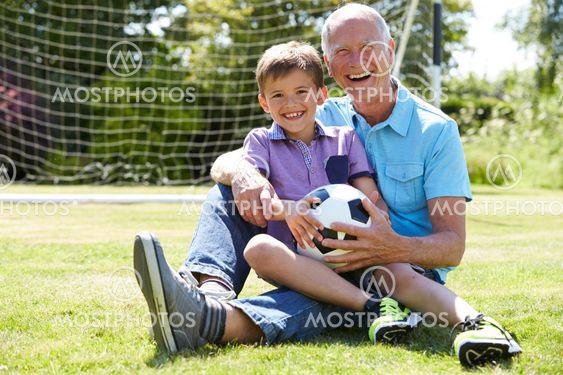 Grandfather And Grandson Playing Football In Garden