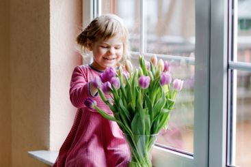 Little girl sitting by window with tulip flowers...