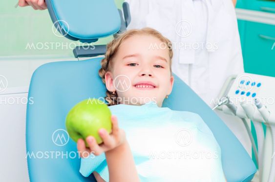 girl in the dentist's chair shows a green apple