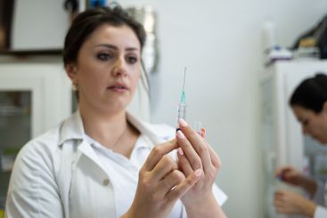 A focused nurse in a white lab coat carefully prepares a...