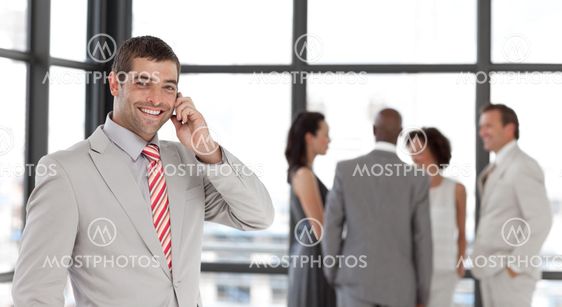 Joyful businessman holding a phone at workplace with his colleagues