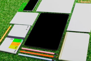 Stationery and digital tools arranged on green grass for...