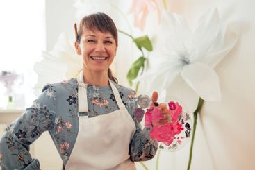 A young woman smiles and holds a palette of paints. A...