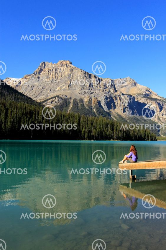 Young woman sitting on a pier at Emerald Lake, Yoho...