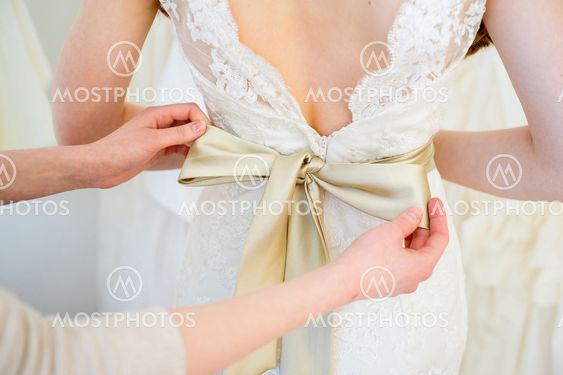 Bridesmaid tying bow on wedding dress
