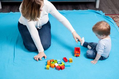 Toys on the floor and baby boy with her mother playing...