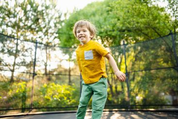 Little boy jumping on a trampoline in a backyard on warm...