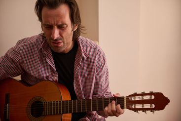 Man playing acoustic guitar passionately in indoor...