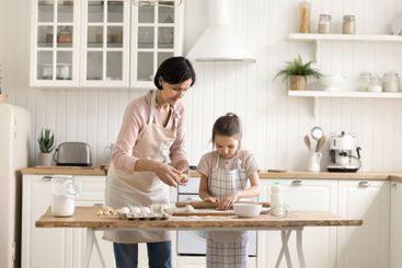 Focused little girl roll dough with help of elderly granny