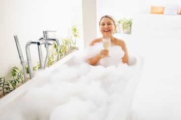 A young woman laughs and takes a bath with fluffy foam....