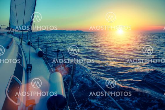 Sailing yacht glides at twilight on water surface of the sea.