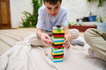 Boy concentrating while building a colorful tower with...