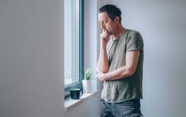 Serious caucasian male looking through window and...