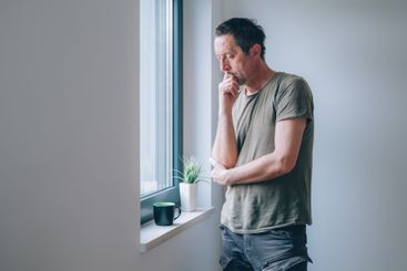 Serious caucasian male looking through window and...