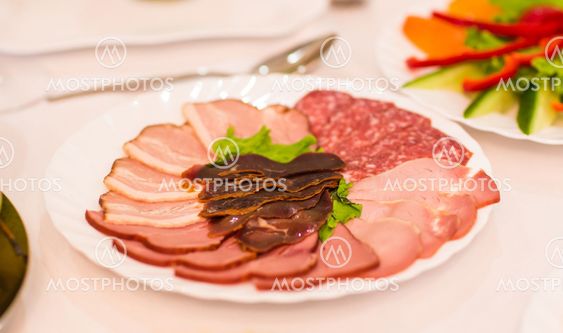 platter of sliced ham,salami and cured meat with vegetable decoration on festive table.