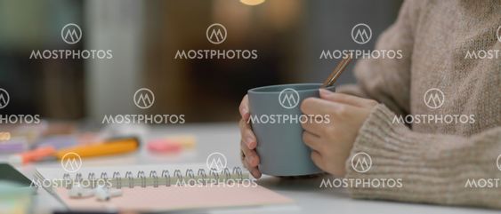 Female student holding cup while sitting at study table