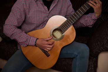 Person Playing Acoustic Guitar Indoors Wearing Checkered...