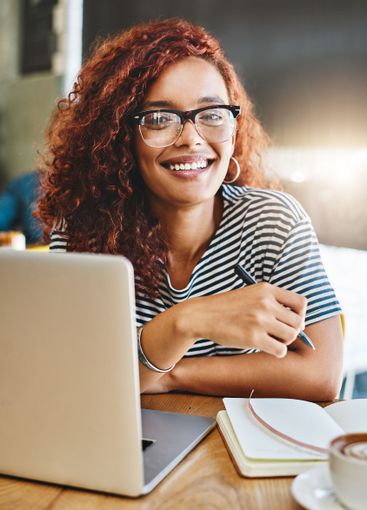 Woman, laptop and notebook with smile at cafe, portrait...