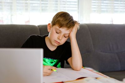 Upset school kid boy making homework during quarantine...