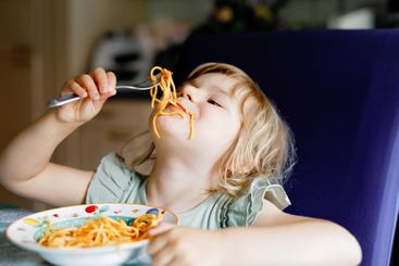 Adorable toddler girl eat pasta spaghetti with tomato...