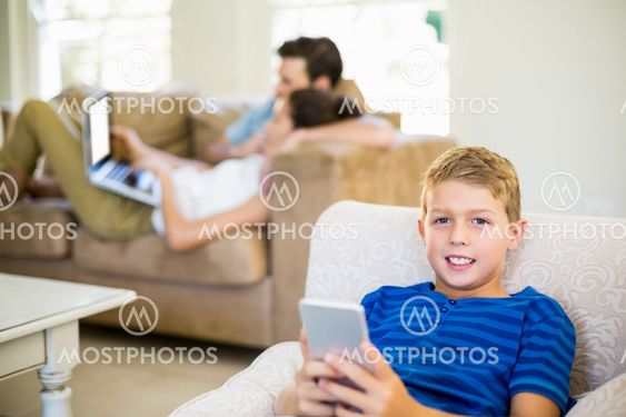 Portrait of boy sitting on sofa and using mobile phone