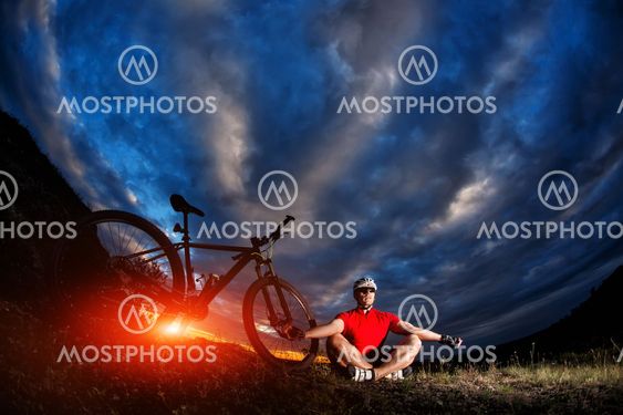 Man cyclist is engaged in yoga on a sunset