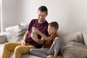 Dad and son sit together on cozy sofa with smartphone