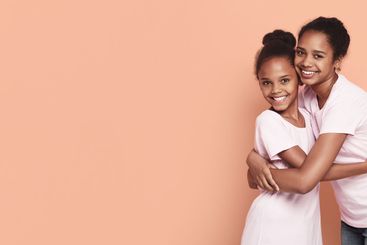 Two african girlfriends cuddling over pink background