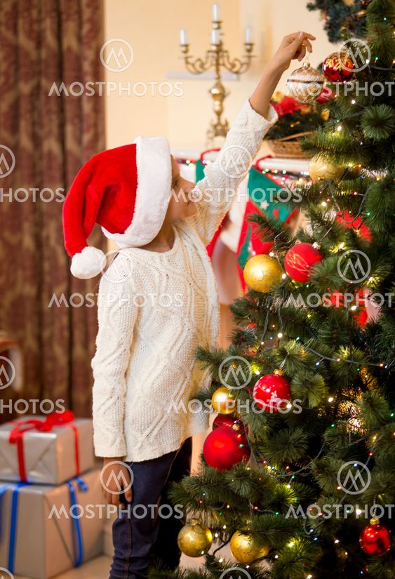 Little girl in Santa's hat putting ball on top of...