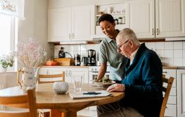 Smiling female caretaker serving breakfast to senior man sitting at dining table in kitchen