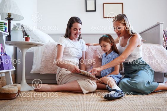 Same Sex Female Couple Sitting On Bedroom Floor Reading...