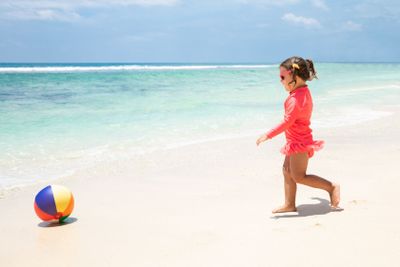 Toddler Girl Playing With Ball Near The Seashore On Beach