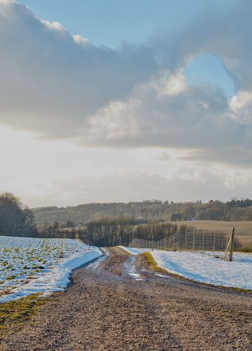 Dirt road, cloudy sky and fence with snow terrain of...