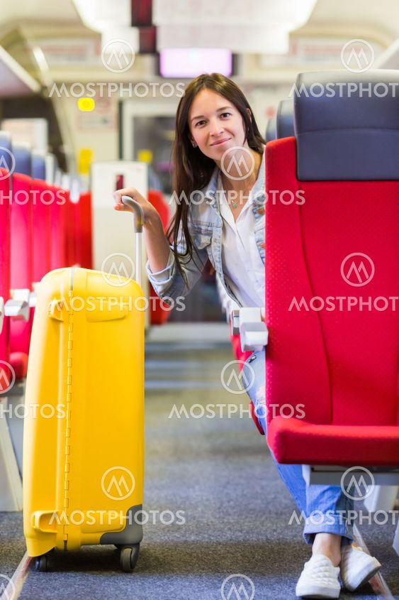 Young happy girl traveling by train with big yellow luggage