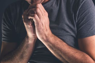 Christian man praying to God in dark room with clasped...