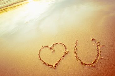 Romantic beach message written in sand during sunset on...