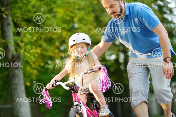 Happy father teaching his little daughter to ride a...