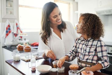 Woman, kid and decorate dessert in home for love,...