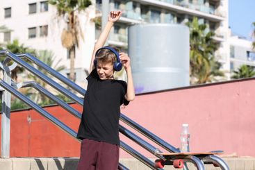 Handsome teenager standing with skateboard and listening...