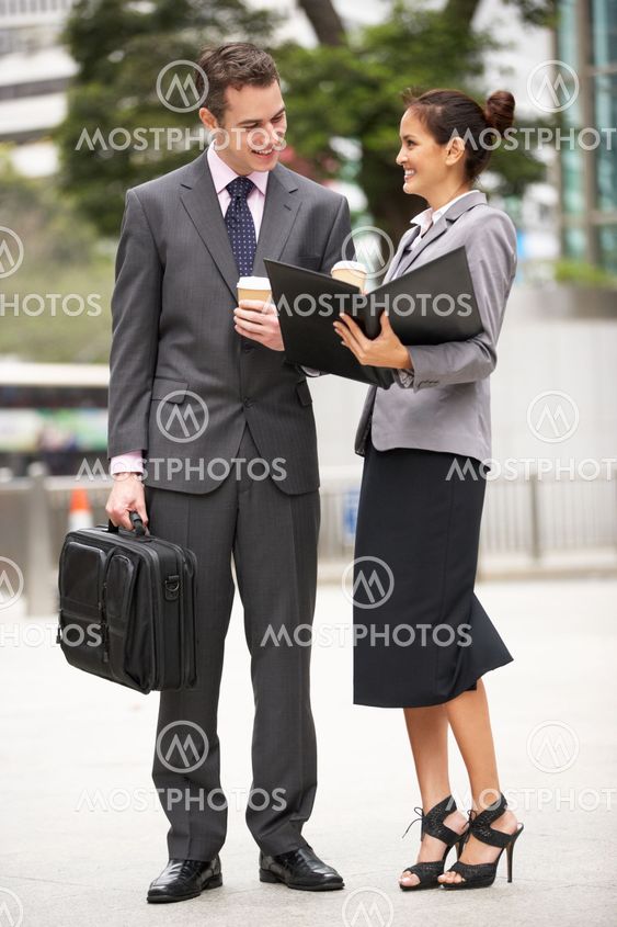 Businessman And Businesswoman Discussing Document In Street Holding Takeaway Coffee