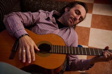 Man relaxing while playing acoustic guitar indoors on a...