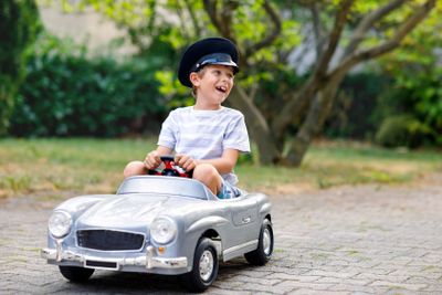 Happy kid boy playing with big old toy car in summer...