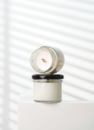 Candle With Extinguished Flame Resting on Glass Jar Near...